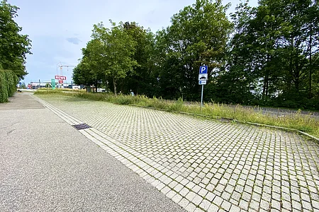 Parkplatz mit Pflastersteinen und Parkverbotsschild für Lkw neben Gehweg und Bäumen unter bewölktem Himmel