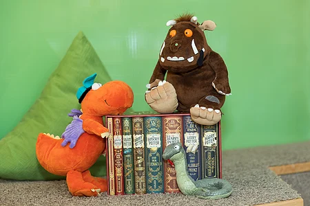Plüschtiere und sieben Harry-Potter-Bücher auf Teppich vor grünem Hintergrund und Kissen.