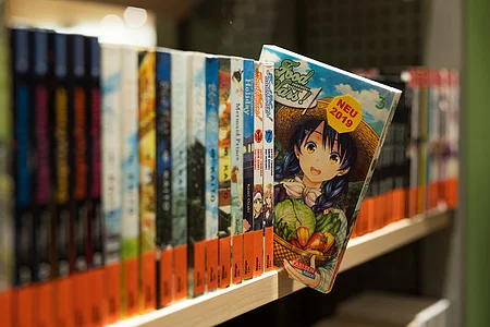 Regal mit Manga-Büchern, ein Band mit Anime-Figur und Gemüse auf dem Cover steht schräg heraus.