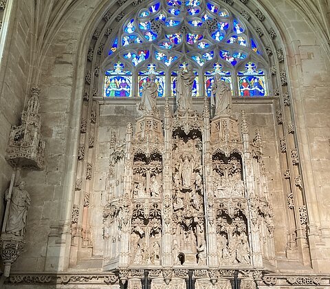 Gruppe von Menschen vor einem gotischen Altar mit Figuren und buntem Kirchenfenster im Hintergrund