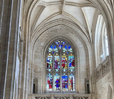 Gotisches Kirchenfenster mit bunten Glasmalereien und steinernen Gewölbebögen im Innenraum einer Kirche