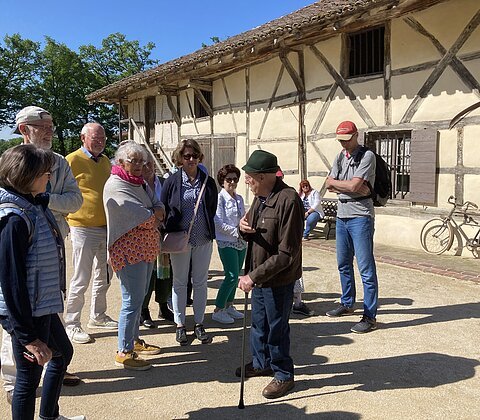 Gruppe von Menschen bei einer Führung vor einem Fachwerkhaus an einem sonnigen Tag mit blauem Himmel.