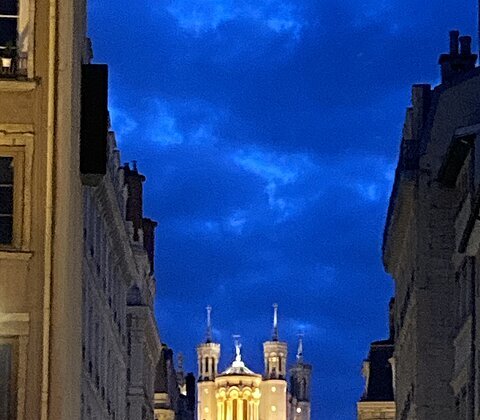 Blick auf beleuchtete Basilika über Häusern bei Nacht unter bewölktem Himmel.