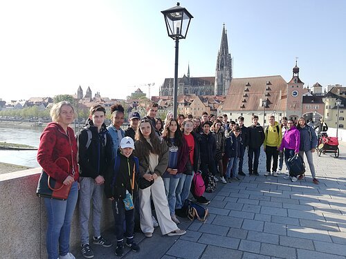 Gruppenfoto von Jugendlichen und Erwachsenen auf einer Brücke mit Blick auf eine Stadt und einen Dom im Hintergrund.