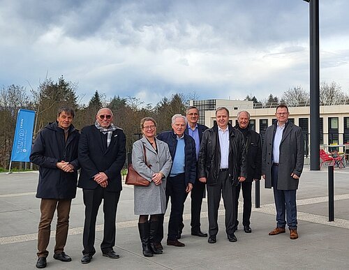 Acht Personen stehen vor einem modernen Gebäude mit der Aufschrift „Campus Région du Numérique“ bei bewölktem Himmel.