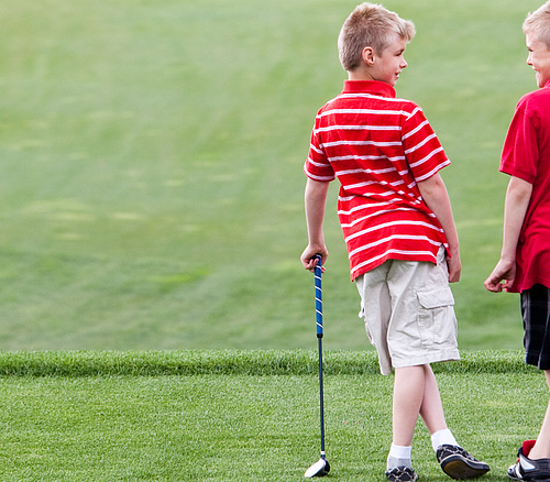 Zwei Jungen in roten Hemden stehen auf einem Golfplatz, einer hält einen Golfschläger.