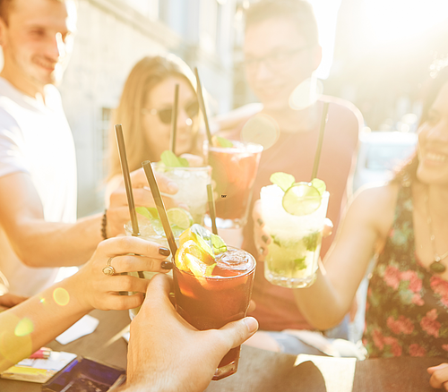 Gruppe von Menschen stößt mit verschiedenen Cocktails bei Sonnenschein an, Fokus auf den Getränken.
