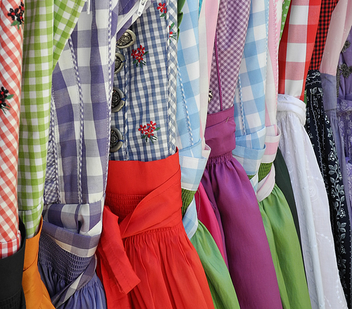 Reihe bunter Trachtenkleider mit karierten Mustern und bestickten Details, hängend nebeneinander.