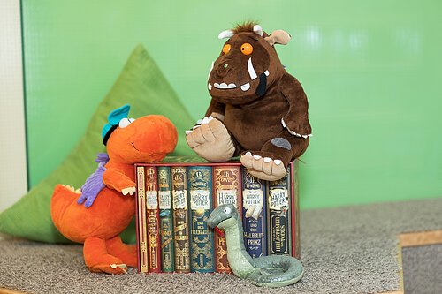 Harry-Potter-Buchreihe mit drei Kuscheltieren, darunter ein Drache, ein Monster und eine Schlange, auf Teppichboden.