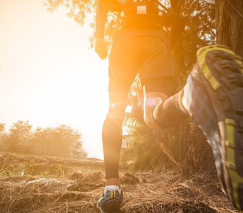 Person läuft auf Waldweg bei Sonnenaufgang, Fokus auf Beine und Laufschuhe von hinten unten