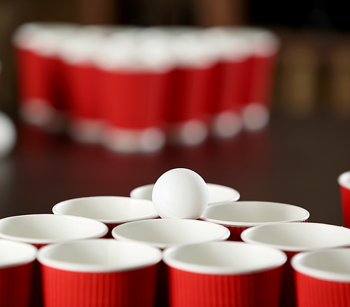 Roter Becherpyramide mit einem weißen Tischtennisball darauf, unscharfe Becher im Hintergrund.