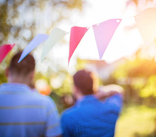 Zwei unscharfe Personen im Freien mit bunter Wimpelkette und Sonnenlicht im Hintergrund.
