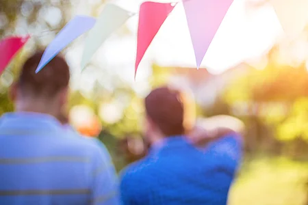 Zwei unscharfe Personen im Freien mit bunter Wimpelkette und Sonnenlicht im Hintergrund.
