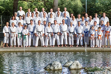 Gruppenfoto von 45 Personen in Karateanzügen mit verschiedenen Gürtelfarben vor einem Teich und Bäumen im Hintergrund.