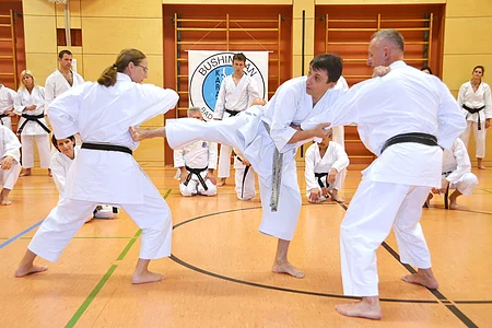 Karate-Training mit mehreren Personen in weißen Anzügen und schwarzen Gürteln in einer Sporthalle.