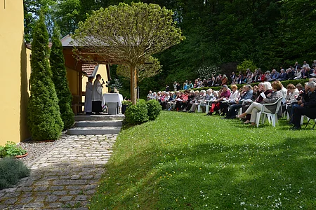 Außenveranstaltung mit zwei Geistlichen an einem Altar und einer großen sitzenden Zuhörerschaft auf einer Wiese.