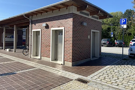 Gebäude mit drei Türen, Parkplatz mit Behindertenparkplatzschild und mehreren Autos im Hintergrund.