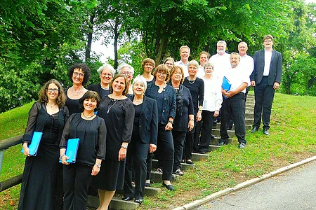 Gruppenfoto von 18 Personen in schwarzer und weißer Kleidung auf einer Treppe im Freien vor Bäumen und Gras.