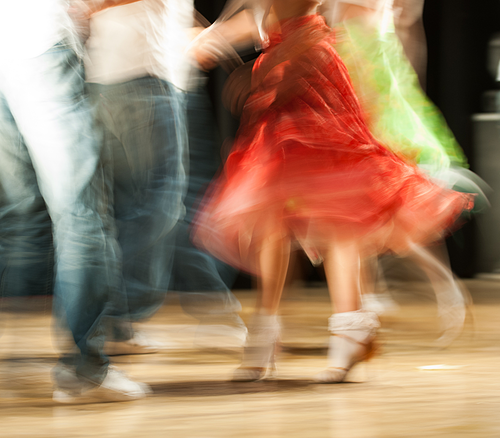Tanzende Personen mit verschwommenen Beinen und rotem Rock in Bewegung auf Holzboden