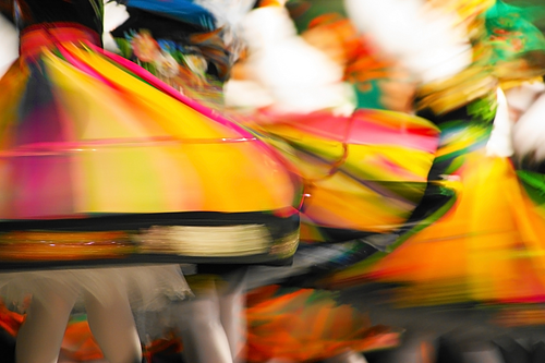 Tanzende Personen in bunten, sich drehenden Kleidern mit Bewegungsunschärfe.