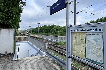 Bahnsteig mit Treppe zum Untergrund, Fahrplan-Information und Schild „zu den Zügen“ an Gleisen
