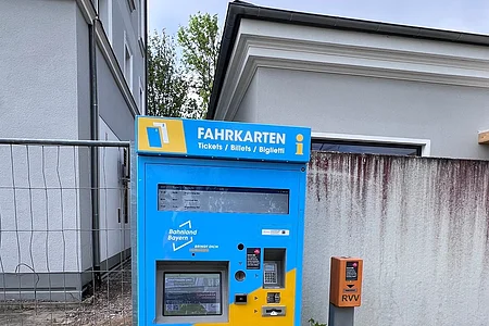 Blauer und gelber Fahrscheinautomat steht auf gepflastertem Boden