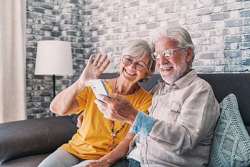 Happy retired family couple using mobile phone for video call together, talking to relations, getting good news, having fun, smiling and laughing. Carefree mature pensioners chatting online on cell