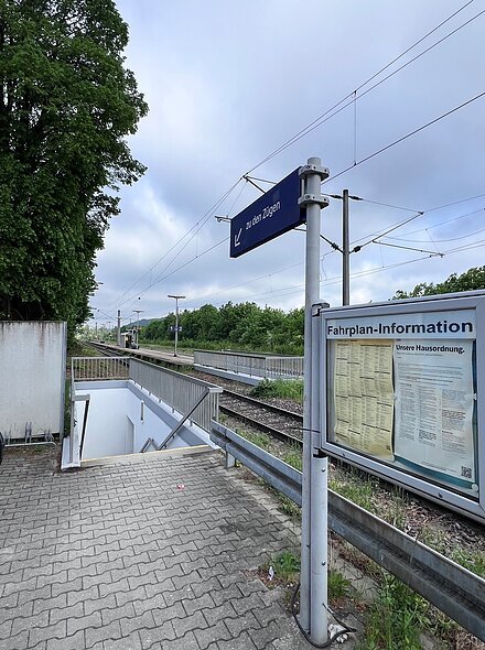 Bahnsteig mit Treppe zum Untergrund, Fahrplan-Information und Schild „zu den Zügen“ an Gleisen