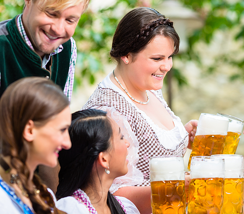 Gruppe von vier Personen in Trachten, die Bierkrüge mit Schaum in der Hand halten und lächeln.