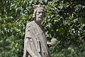 Steinerne Statue eines bärtigen Königs mit Krone und Kugel in der rechten Hand umgeben von grünen Pflanzen.