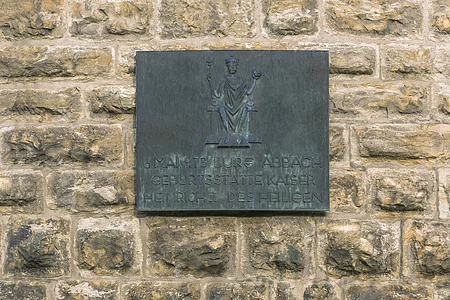 Bronzetafel an einer Steinmauer mit der Aufschrift zur Geburtsstätte Kaiser Heinrich II. in Bad Abbach.