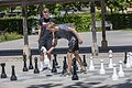 Zwei junge Männer spielen im Freien Schach mit übergroßen Figuren auf einem Schachbrett aus Stein.