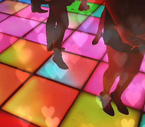 Disco Tanzfläche Beine von Personen auf einem bunten, beleuchteten Tanzboden mit Herzlichtreflexionen.