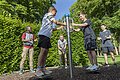 Fünf Jungen spielen an einem Outdoor-Drehgerät in einem Park mit grünen Büschen und Bäumen.