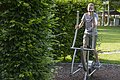 Junge trainiert auf einem Outdoor-Fitnessgerät in einem Park mit grünen Hecken und Rasen.