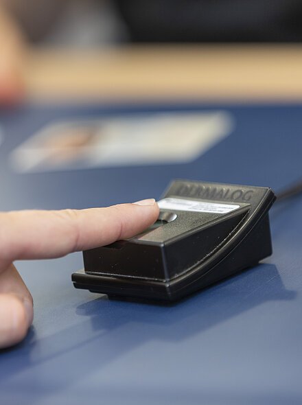 Markt Bad Abbach Rathaus Raiffeisenstraße Einwohnermeldeamt Hand legt Finger auf schwarzen Fingerabdruckscanner auf blauem Tisch, unscharfe Hand im Hintergrund