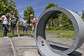 Vier Personen spielen Minigolf auf einem sonnigen Außenplatz mit Betonhindernissen und grüner Umgebung.