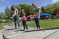 Drei Personen spielen Minigolf auf einem sonnigen Platz mit Bäumen und Sonnenschirmen im Hintergrund.