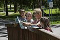 Vier Kinder lesen gemeinsam Broschüren an einem Holzzaun im Park bei Sonnenschein.
