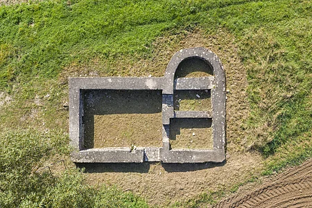 Luftaufnahme von rechteckigen und halbrunden Steinmauern einer Ruine auf Grasboden.