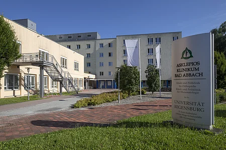 Außenansicht des Asklepios Klinikums Bad Abbach mit Eingangsbereich und Beschilderung bei klarem Himmel.