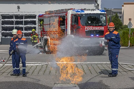 Jugendliche Feuerwehrleute löschen mit Wasser einen Übungsbrand vor einem Feuerwehrauto.