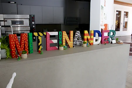 Bunte Buchstaben auf einer Theke bilden das Wort „MIENANDER“ mit kleinen Pflanzen und Figuren davor.