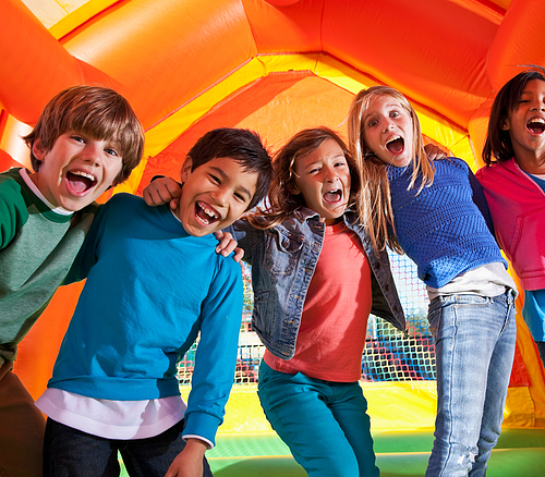 Fröhliche Kinder in einer Hüpburg Fünf Kinder stehen eng zusammen und lachen in einem orangefarbenen Hüpfburg-Spielplatz.
