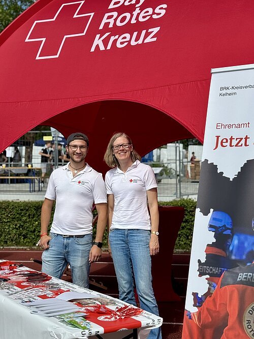 Mitarbeitende stellen die Arbeit des BRK vor Zwei Mitarbeitende vor einem BRK-Zelt am Infostand