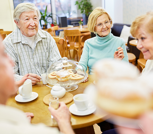 Senioren in einer Kaffe-Runde Ältere Menschen sitzen an einem Tisch mit Kaffee und Keksen in einer hellen Cafeteria.