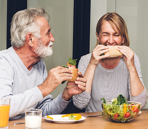 Mittagessen miteinander Älterer Mann und Frau essen Sandwiches an einem Tisch mit Salatschüssel und Getränken.