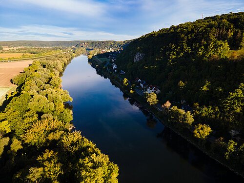 Donauaue Fluss mit bewaldeten Ufern und Häusern am Hang unter blauem Himmel in der Landschaft