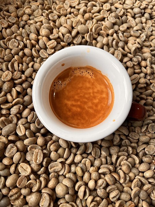 Weiße Espressotasse mit Espresso auf rohen, grünen Kaffeebohnen liegend, Draufsicht.