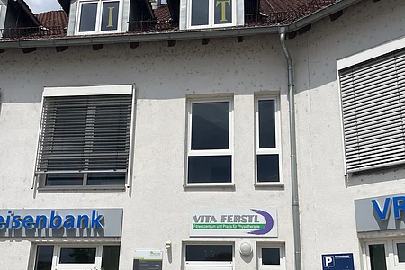 Fassade eines Gebäudes mit Geschäftsschildern und drei Dachgauben mit Buchstaben I, T und N in den Fenstern.